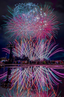 ピンクと白の花火が水面に映り込み幻想的な世界を描く