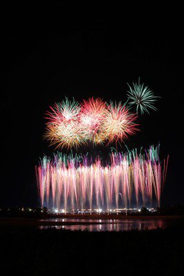 川面に映る光と共に打ち上がる花火の列