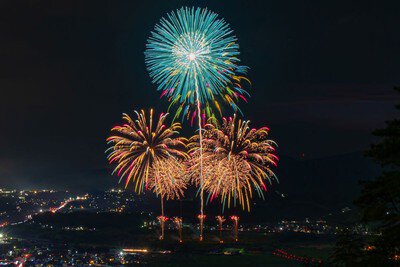 山並みと街明かりを背に咲き誇る花火※画像はイメージ