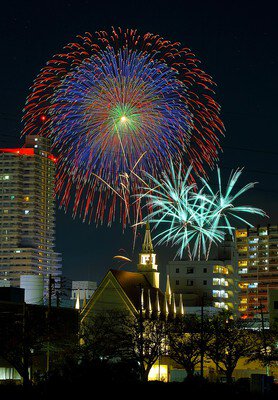 都市の夜景を背景に広がる大輪の華