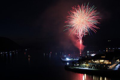港の灯りに寄り添う紅色の花火と静かな海面(※2025年の写真)